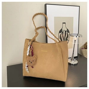 Detail of khaki suede tote bag with braided handles and a brown plush bear charm