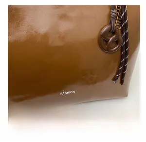 Detail of glossy caramel brown tote bag with white FASHION text and woven lanyard charm
