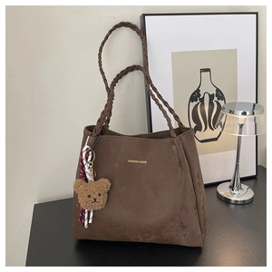 Detail of dark brown suede tote bag with woven strap and cute plush bear charm