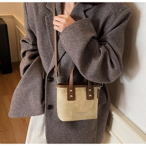 Detail of a beige suede crossbody bag with brown leather handles and gold metal rivets