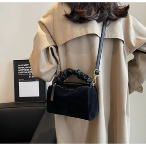 Détail d'un sac cylindre en daim noir avec poignée plissée et bandoulière réglable