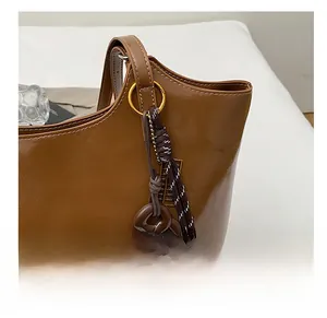 Detail of a brown leather tote bag showing woven rope charms and gold metal hardware