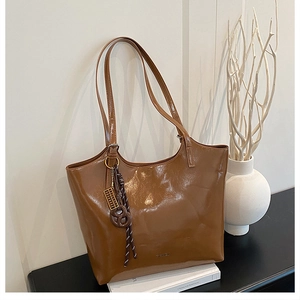 Detail of a brown glossy tote bag featuring a gold ruler charm and elegant slim shoulder straps