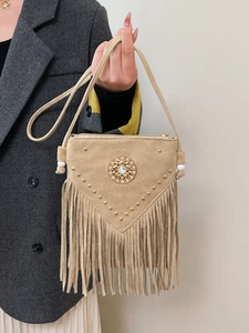 Beige bohemian tassel crossbody bag with gold studs and fringe held by a model