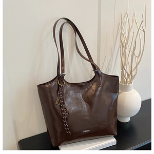 Detailed macro view of the glossy brown leather finish and fashion charm on the tote bag