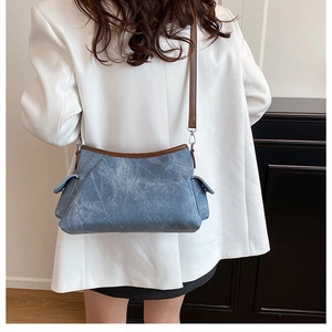 Detail view of denim blue shoulder bag with brown leather trim and side flap pockets