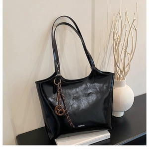 Macro detail of glossy black tote bag with white FASHION print and creative pendant