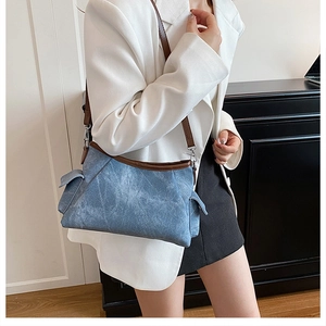 Close-up of blue denim shoulder bag with brown leather trim worn by a model