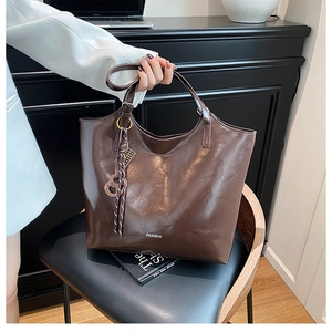 Detail of dark brown tote bag featuring glossy finish, metal ring buckles and tassel charm