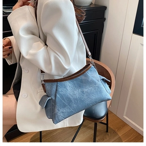 Detail of denim shoulder bag with brown leather trim and unique folded 3D structure