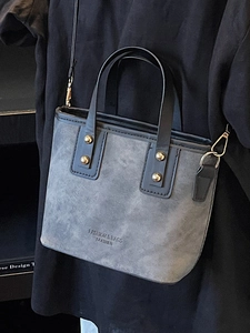Luxury grey suede bucket bag with gold rivets and leather handle shown as crossbody
