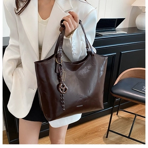 Detail view of large dark brown tote bag with glossy leather finish and fashion heart charm