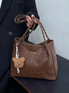 Brown faux leather tote bag with thick woven handle and cute bear charm in hand