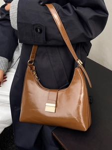 Chic brown patent leather bucket bag with gold buckle on a stylish model's shoulder
