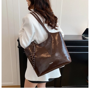 Detail of a large dark brown tote bag in glossy oil wax leather with a fashion tag