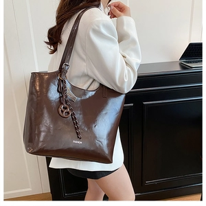 Detail of glossy deep brown tote bag with fashion lettering and metallic charm decor