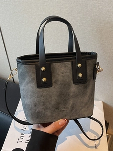 Gray denim tote bag with black leather trim, gold studs and crossbody shoulder strap