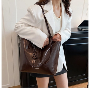 Detail of dark brown glossy leather tote bag with white fashion text and tassel charms