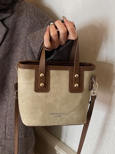 Retro canvas and brown leather crossbody bucket bag held by a model in a warm autumn setting