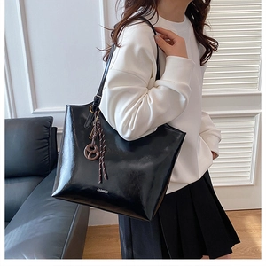 Detail of glossy black tote bag with white FASHION text and decorative striped ribbon charm