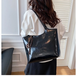 Detail view of large black patent tote bag with white fashion text and woven rope charm