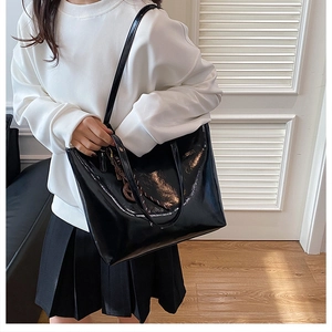 Detail of high-gloss black patent leather tote bag with elegant silver ring charm