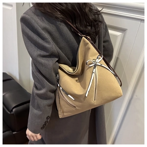 Detail of camel tote bag with asymmetric zipper and bow charm worn with a blazer