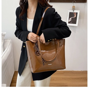 Detail of a brown glossy leather tote bag featuring a decorative knot charm and text
