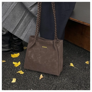 Detail of dark brown faux suede tote bag with braided handles on autumn leaves ground