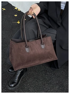 Detail of dark brown suede tote bag featuring smooth leather handles on grey stone background