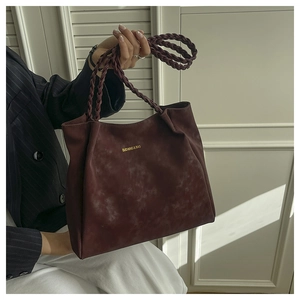 Detail of burgundy faux suede tote bag featuring braided handles and gold logo