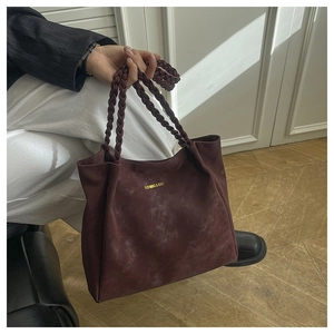 Detail der burgunderroten Wildledertasche mit geflochtenen Griffen und Goldlogo