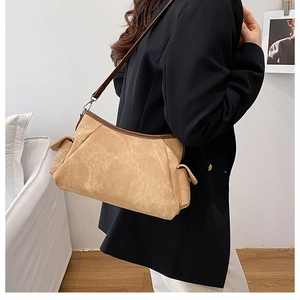 Detail of khaki textured crossbody bag with brown leather trim worn by model in black blazer