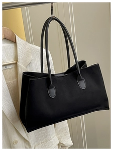 Minimalist black suede tote bag detail hanging against a stylish white blazer background