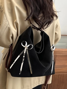 Fashionable black tote bag with cow print bow detail shown on model in a trench coat