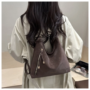 Détail d'un sac cabas marron mat avec fermeture éclair latérale et pompon à l'épaule