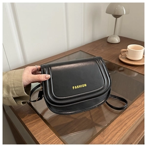 Detail of a black semi-circle crossbody bag with yellow FASHION text on a wood table