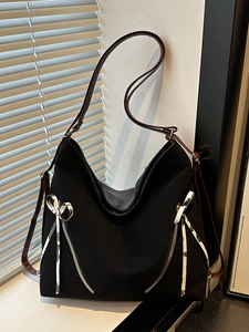 Large black canvas tote bag with brown straps and stylish bow zipper pulls on white wall
