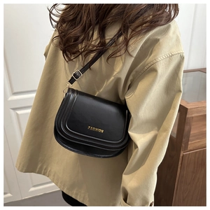 Detail of black matte leather saddle bag featuring gold Fashion lettering and adjustable strap