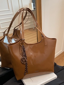 Large brown glossy tote bag for women with fashion charms shown in a mirror reflection