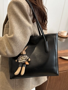Large black leather tote bag for autumn with bunny charm, styled on a model's shoulder