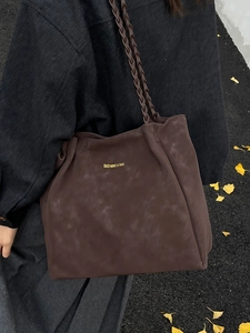 Large brown suede tote bag with woven handles and gold logo shown in autumn setting