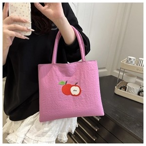 Detailed view of pink nylon tote bag featuring red apple embroidery and top handles