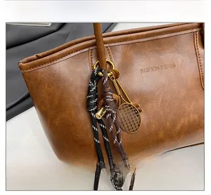 Detail of brown leather tote bag with braided rope charm and metal tennis racket pendant