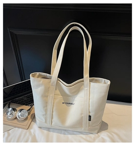 Macro detail of beige canvas tote bag with Be Yourself slogan and shoulder strap