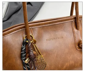 Close-up of brown faux leather tote with golden tennis racket charm and braided detail