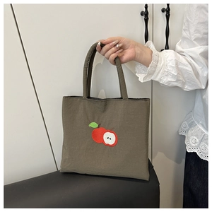 Close-up of nylon tote bag featuring red apple embroidery detail and portable handle