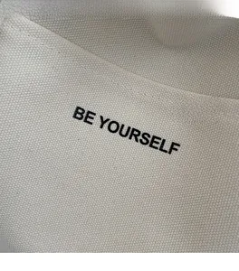 Detailed close-up of cream canvas texture with bold BE YOURSELF printed lettering