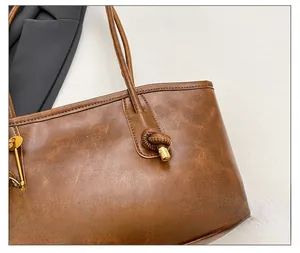 Macro detail of brown leather tote bag showing fine stitching and metal ornament