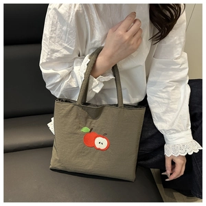 Close-up of embroidered red apple slice on olive green nylon tote bag held by model